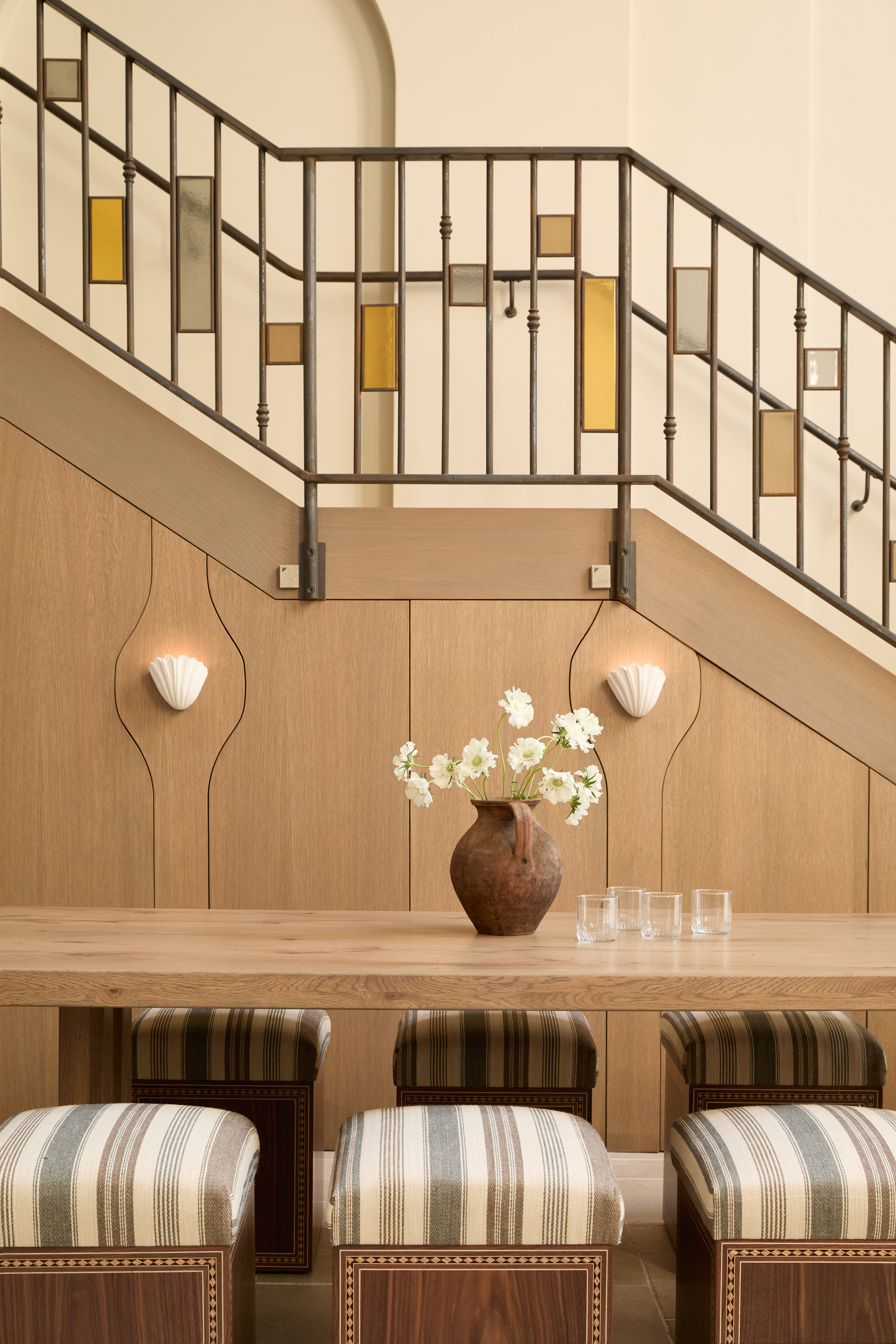 A warmly furnished restaurant with butter and ochre plaster walls, wrought iron chairs with neutral cushions, statement ceilings in brick or plaster relif, and stripy furniture paired with plants.