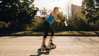 Woman roller blading along path holding water bottle