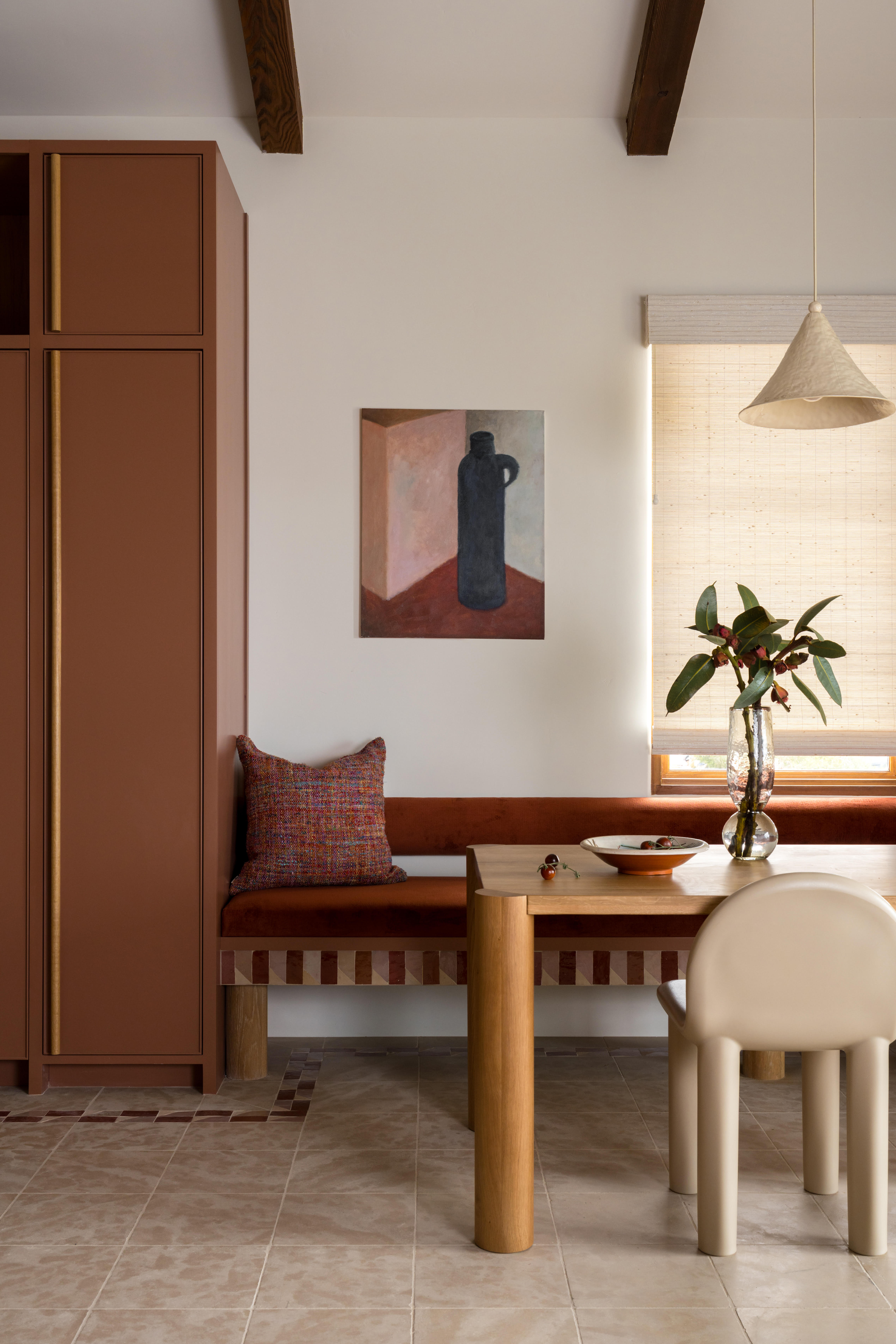 Rust-red kitchen with velvet banquette, wooden table and curved dining chair