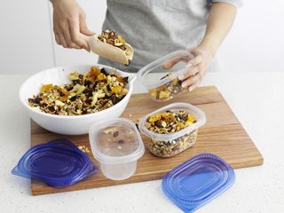 Someone using a wooden food scoop to move granola from a bowl to a jar
