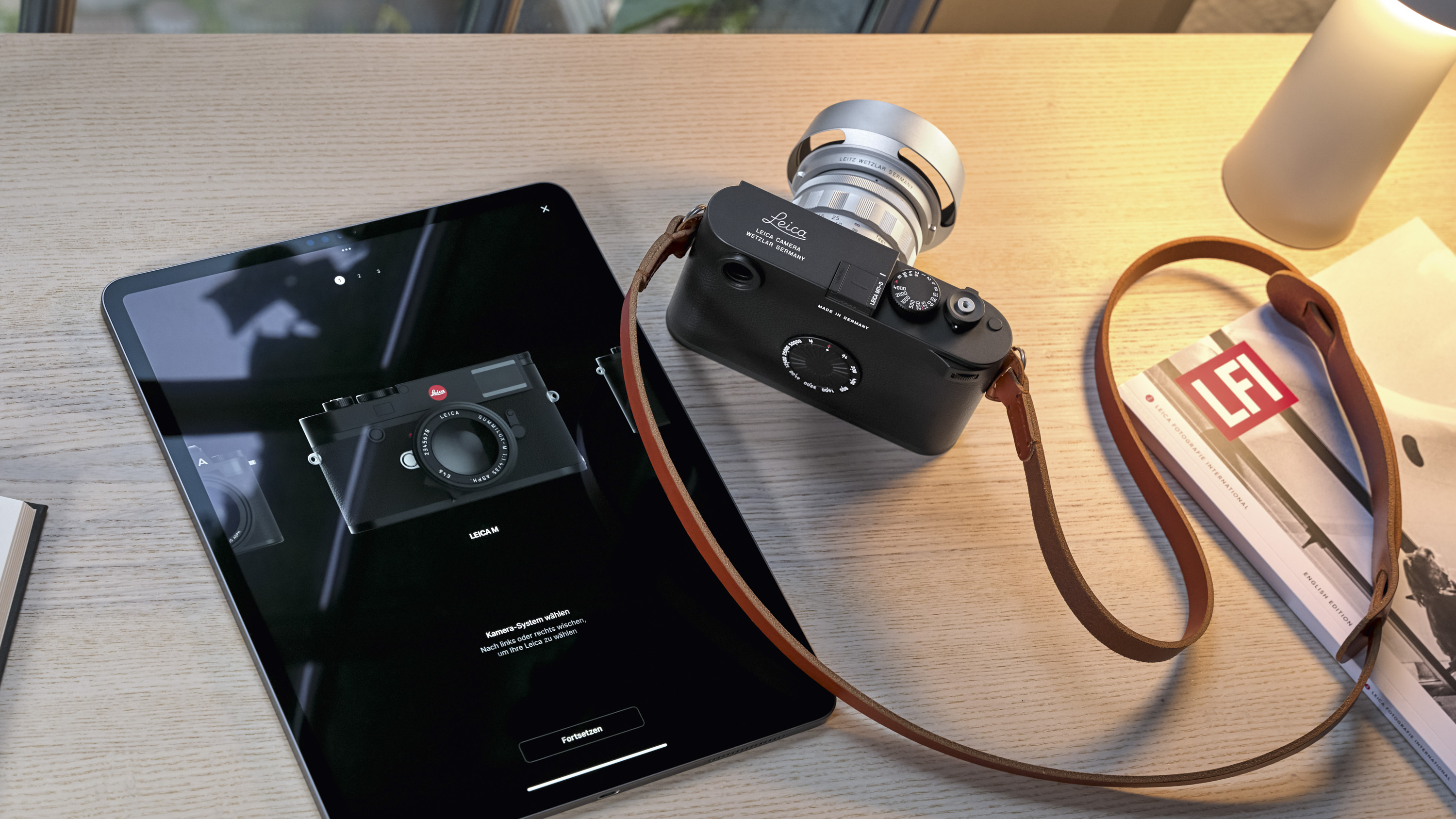 Leica M11-D camera on a table alongside iPad with Foto app disaplyed