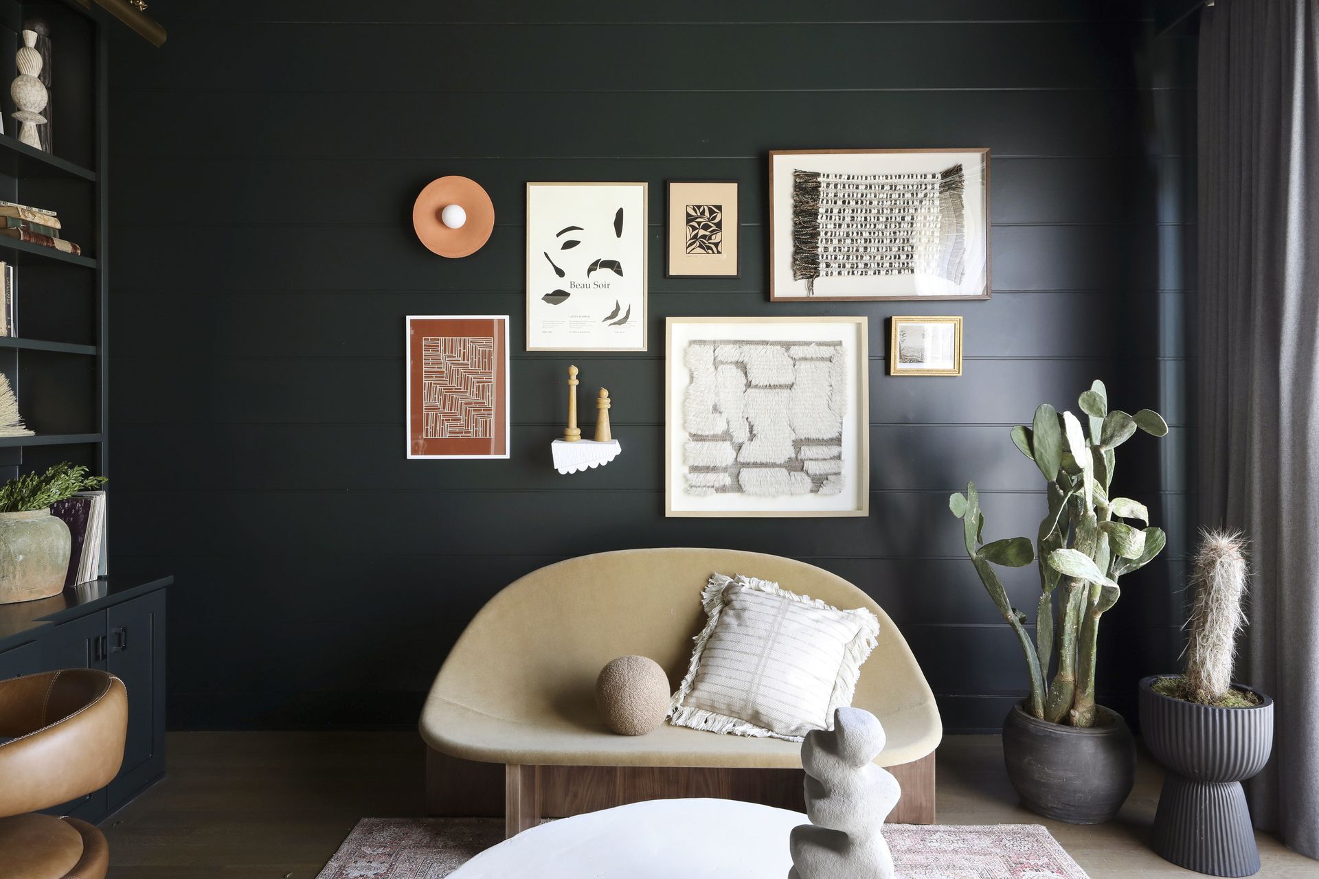 A black living room with a cream sofa and wall sconce