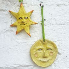 Yellow ceramic sun and moon decorations with faces hanging from green ribbon on white wall