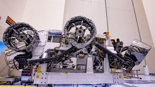 Three of the six flight wheels that will travel to Mars can be seen attached to NASA's Perseverance rover (which is inverted on a handling fixture) on March 30, 2020 at the Kennedy Space Center in Florida. The protective antistatic foil covering the wheels will be removed before launch this summer.