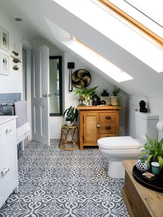 a bathroom with a sloping ceiling, patterned floor tiles, and wooden accessories