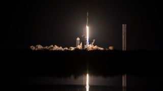 a black-and-white spacex falcon 9 rocket launches into a night sky.