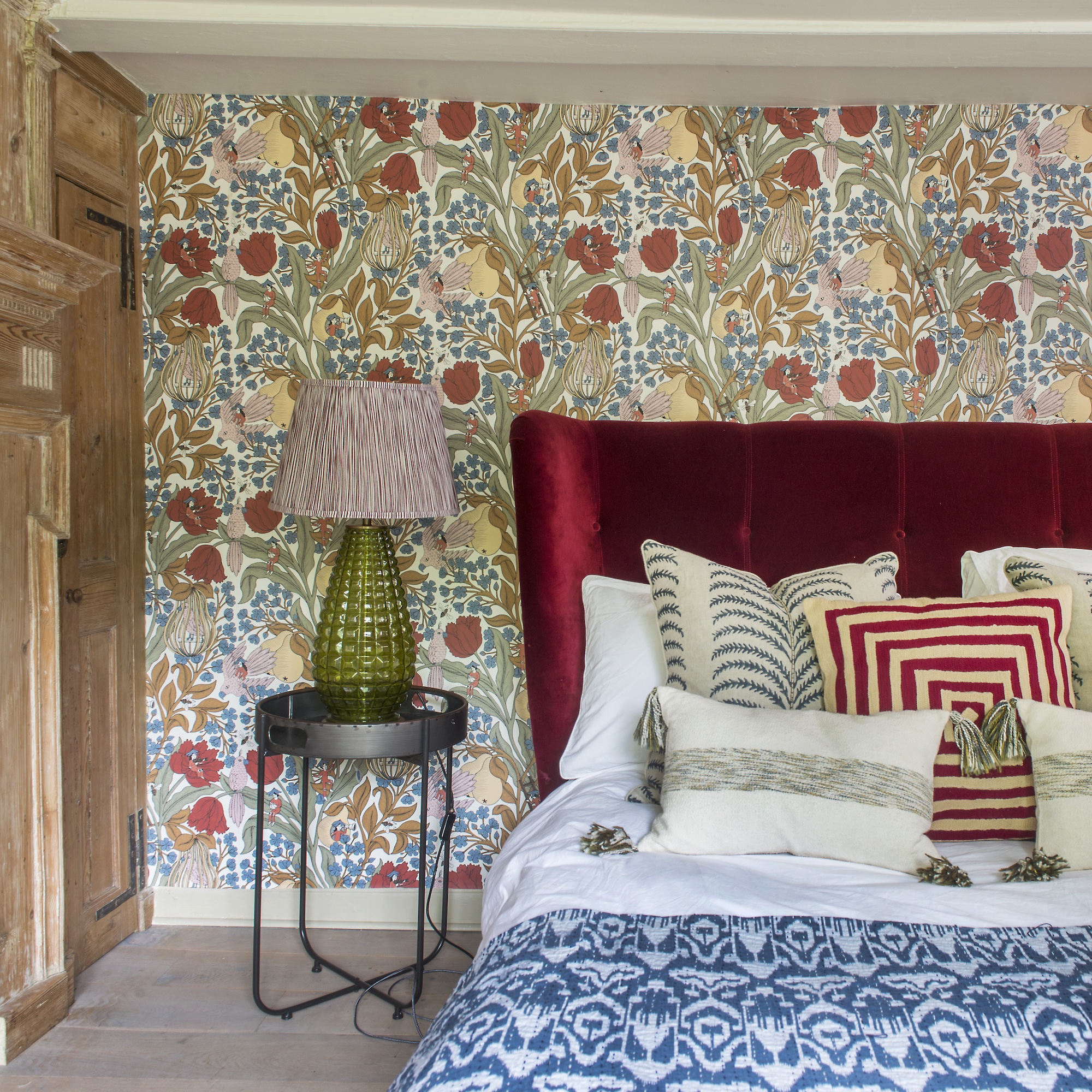 bedroom with large scale poppy wallpaper and red upholstered velvet headboard