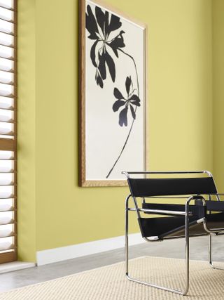 room with yellow walls, artwork of a flower, black leather armchair, and timber shutters on window