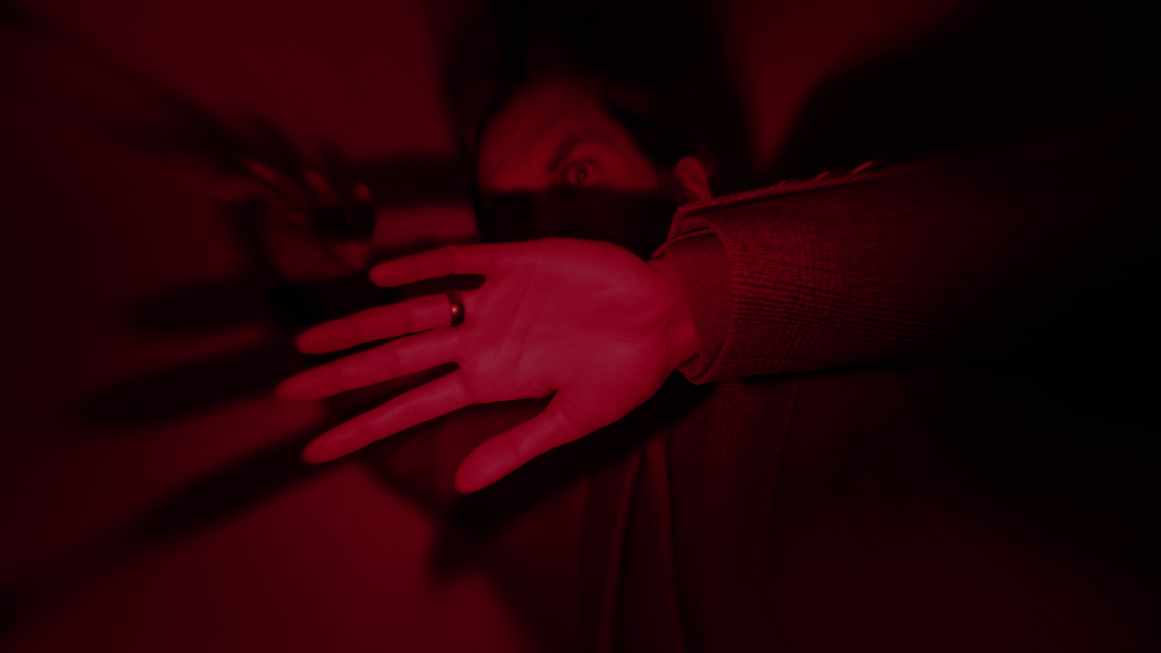 Zrzut ekranu z gry Alan Wake 2 przedstawiający Alana uwięzionego w ciemnym miejscu pod czerwonym światłem