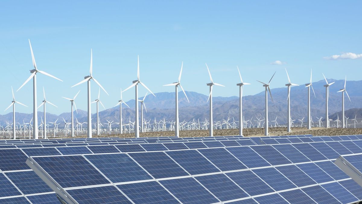 Solar panels in the foreground against a background of dozens of wind turbines and Californian hills in the distance under bright blue skies