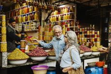 Medium wide shot of smiling senior couple sampling olives at olive stand while exploring the medina of Marrakech during vacation in Morocco