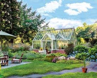 A large greenhouse surrounded by shrubbery and flowers next to an outdoor dining area