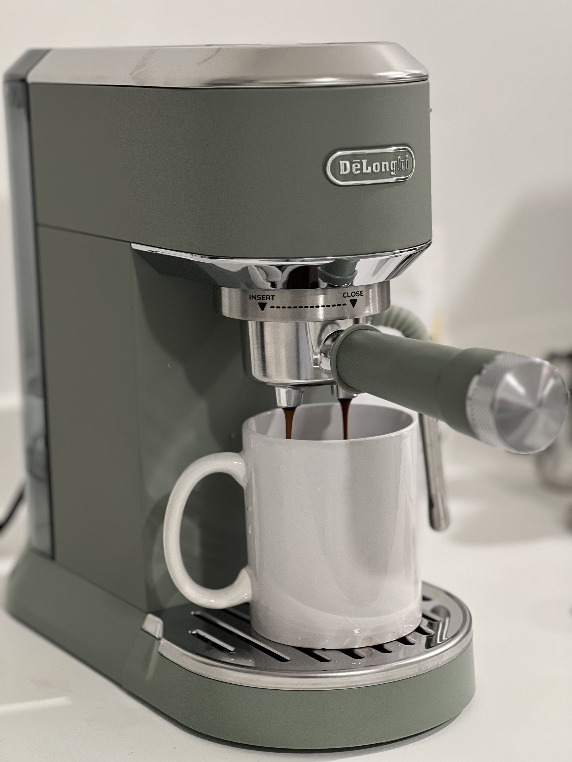 Image of an espresso shot being brewed into a white coffee mug. The machine is a sage green color.