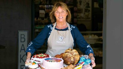 Bakery owner Theresa Hammons in front of her shop holding a collection of her baked goods.