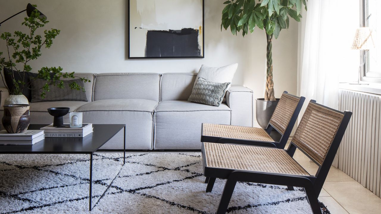 A living room with a grey modular sofa, two rattan accent chairs and a berber-style rug