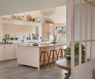 pale pink kitchen with large island, simple half glazed wooden dividers at end of room breaking up space between living areas and kitchen