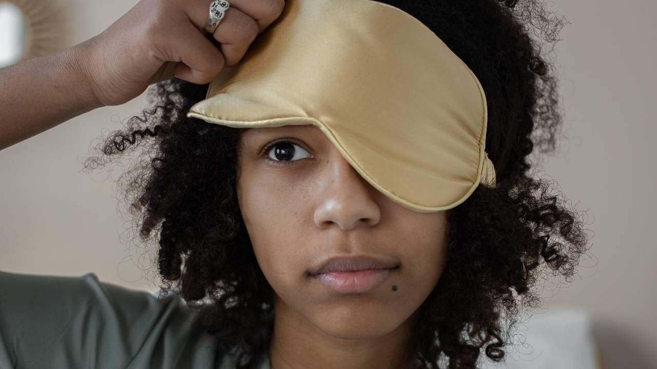 Woman lifting her eye mask up over one eye, sleep &amp; wellness tips