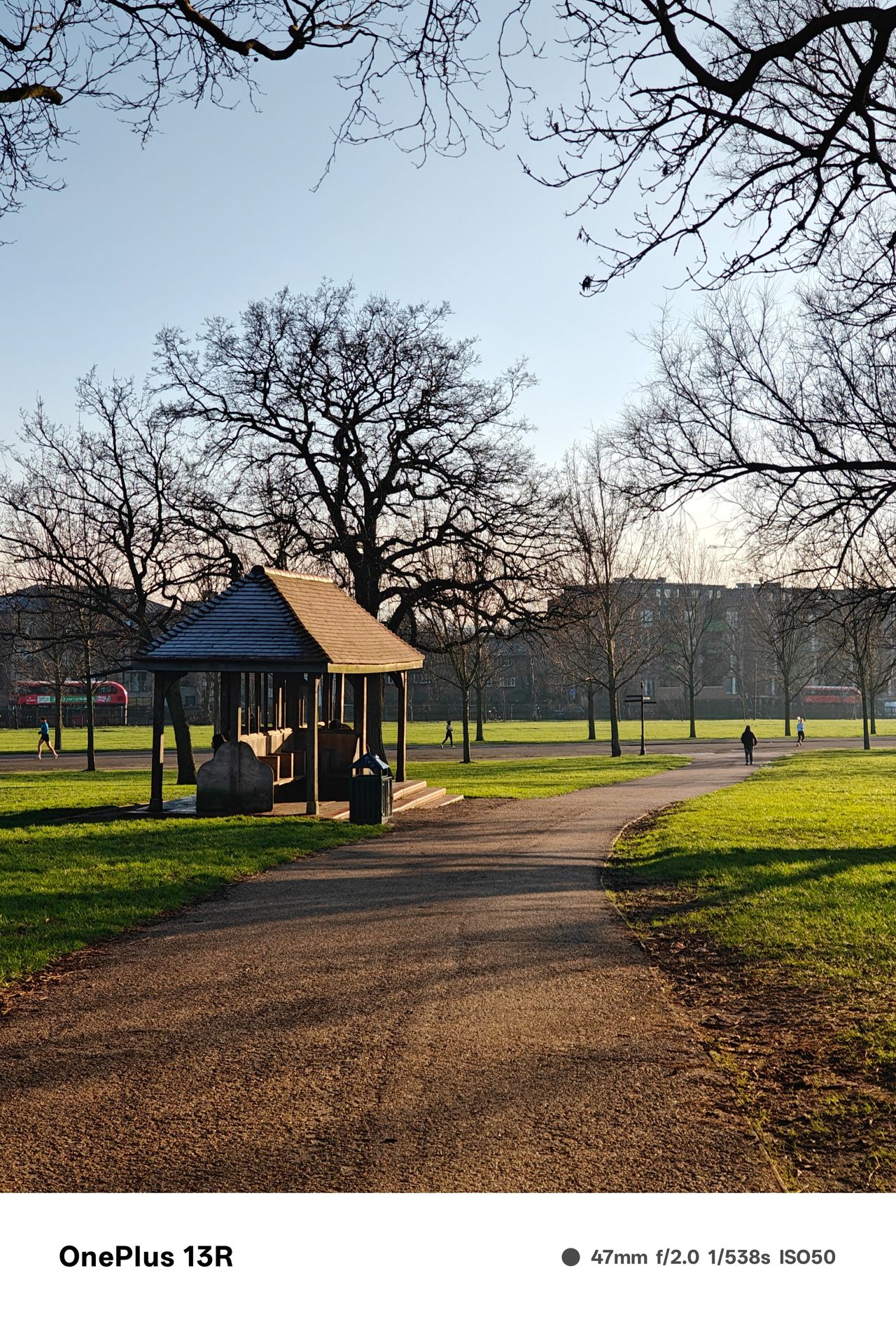 Path past a shelter in a park with green grass and leafless trees