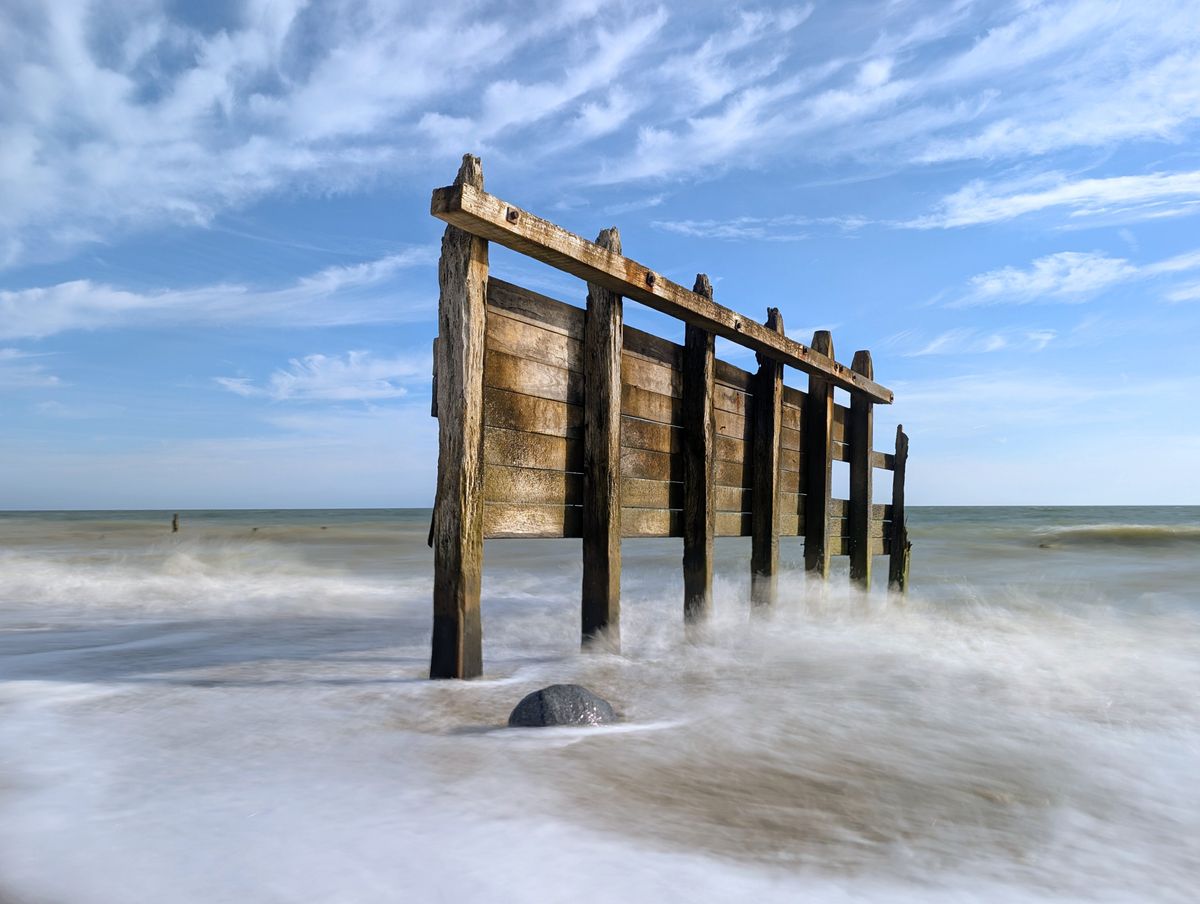 A damaged groyne on a UK beach, the high tide is smashing into it, with the moving water blurred using a long exposure photography technique