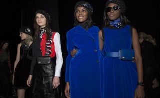 2 Woman back stage wearing all blue jackets and dress with headwear and sunglasses