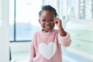 Cute child wearing a pink jumper and glasses smiling at the camera