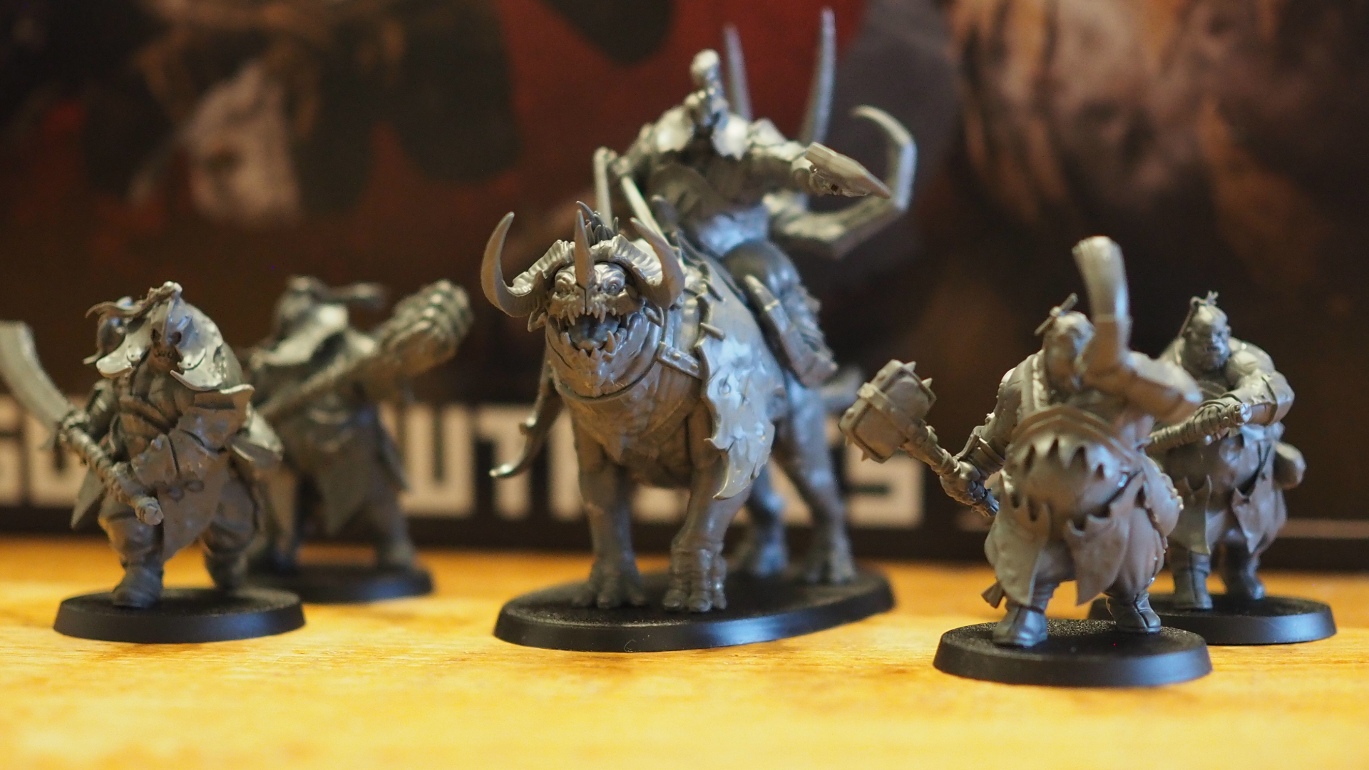 A selection of Ogor Mawtribes miniatures, laid out in a band on a wooden surface