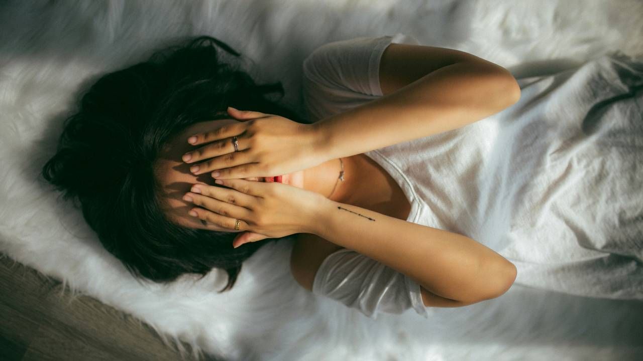 A woman lying on a bed with her hands over her face