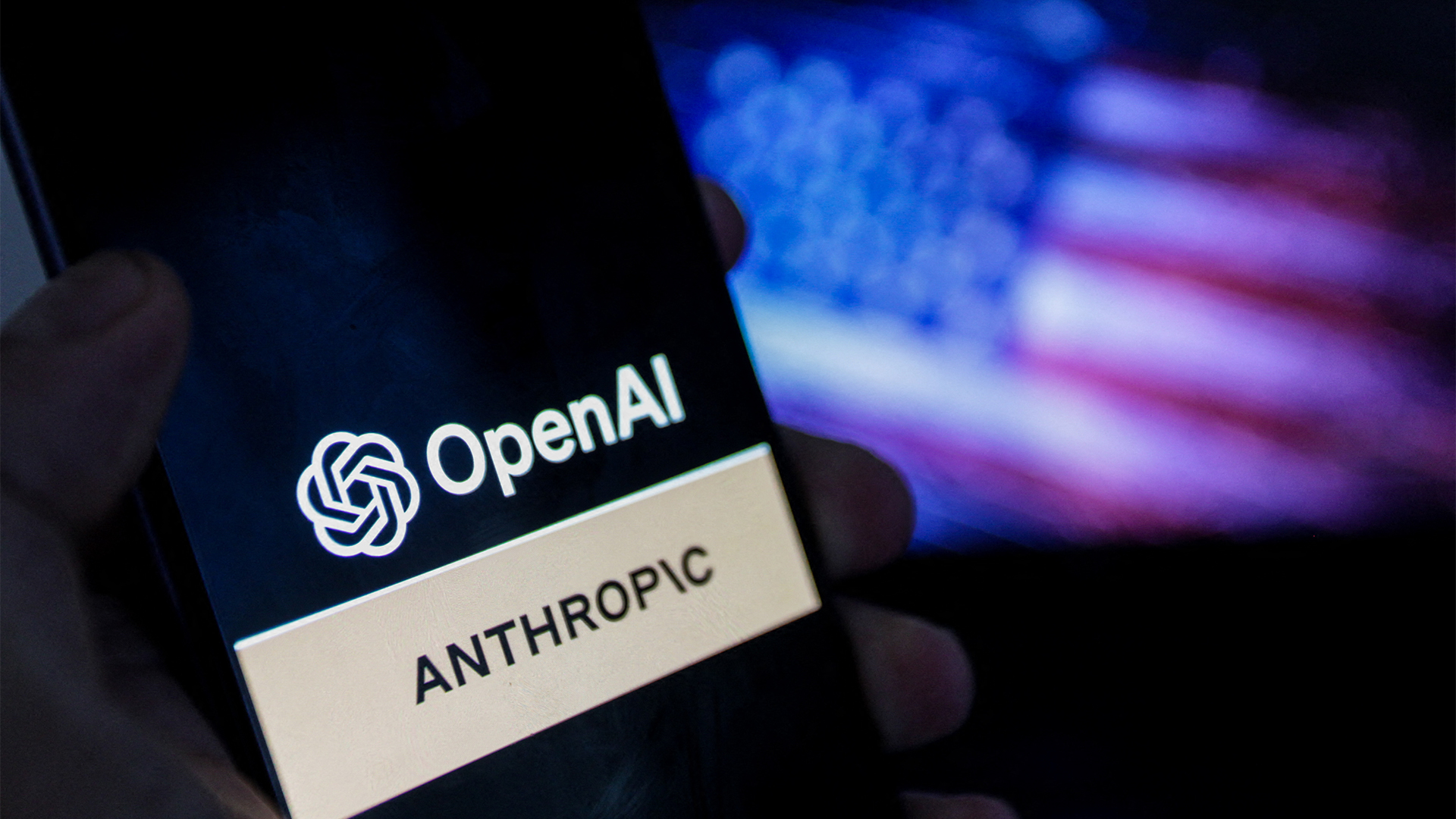 Logos of AI developers Anthropic and OpenAI pictured on a smartphone screen with American flag blurred in background.