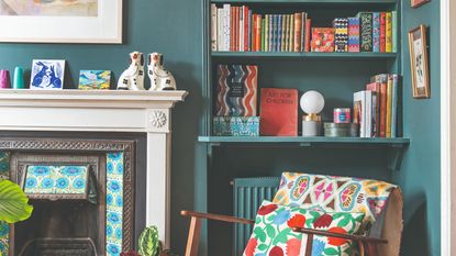 A teal-painted living room with a fireplace and an accent chair in front of an alcove filled with bookshelves