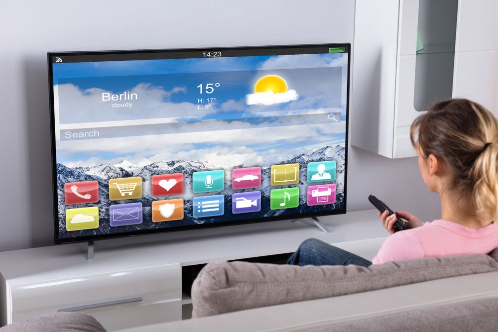 Woman watching large-screen smart TV displaying temperature in Berlin.