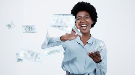 A woman smiles with joy as she tosses money into the air.