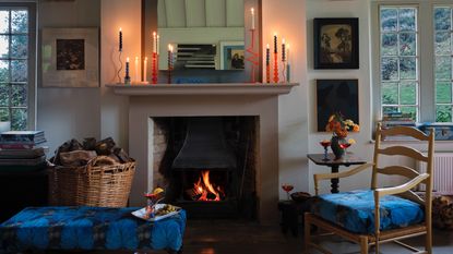 cozy living room with open fire, candles lit on mantle, log basket, armchair, mirror, artwork, Farrow &amp; Ball 