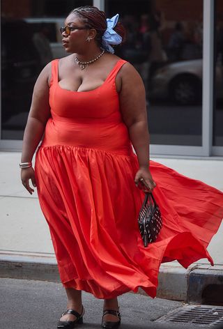 A woman wearing an orange dress with a black studded bag.