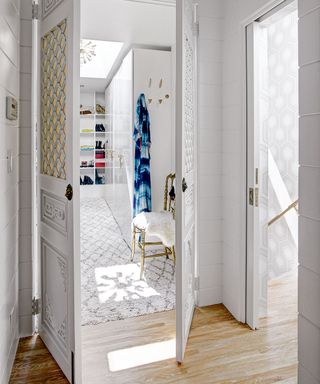 A bright white walk-in wardrobe with gold chair.