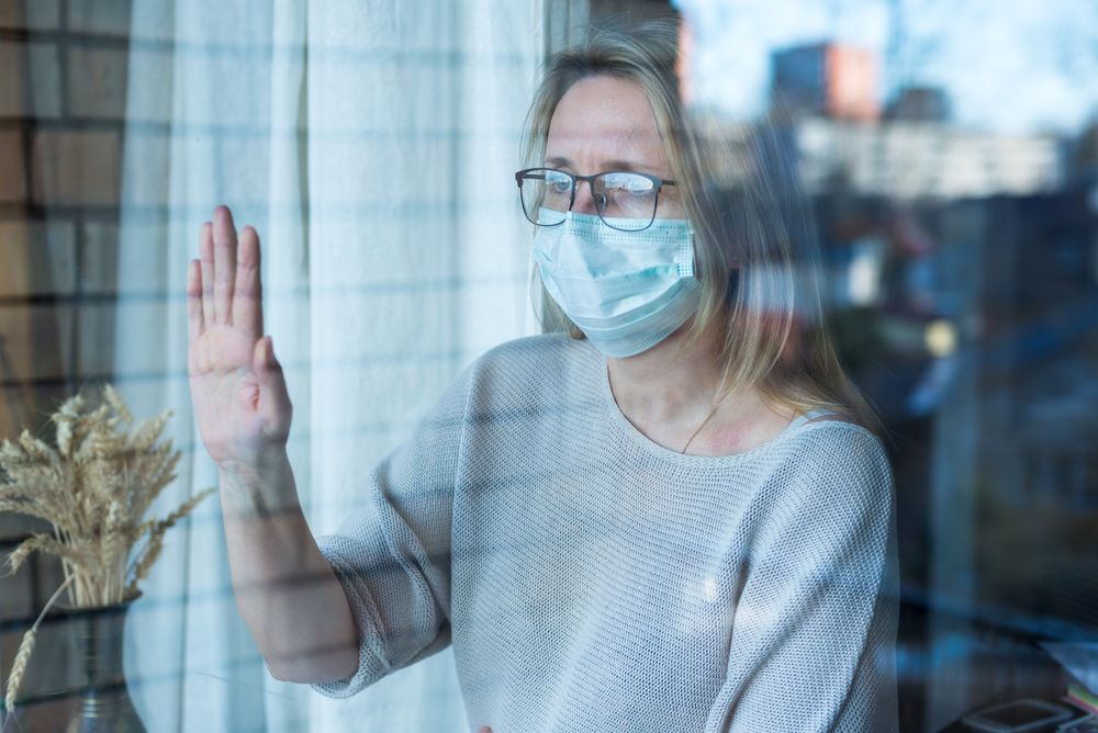 A woman in a facemask during the coronavirus crisis touching and looking out of a window