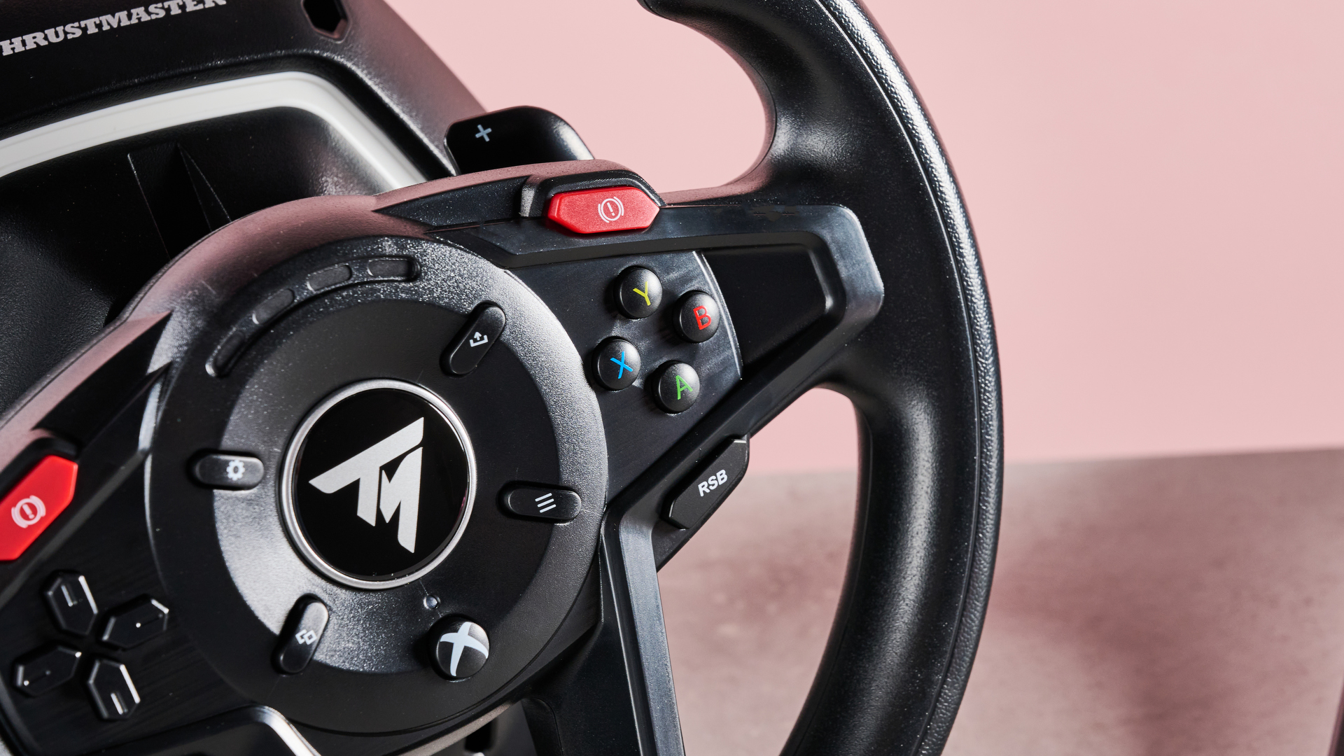 Close-up of buttons on Thrustmaster T128, on desk with pink background
