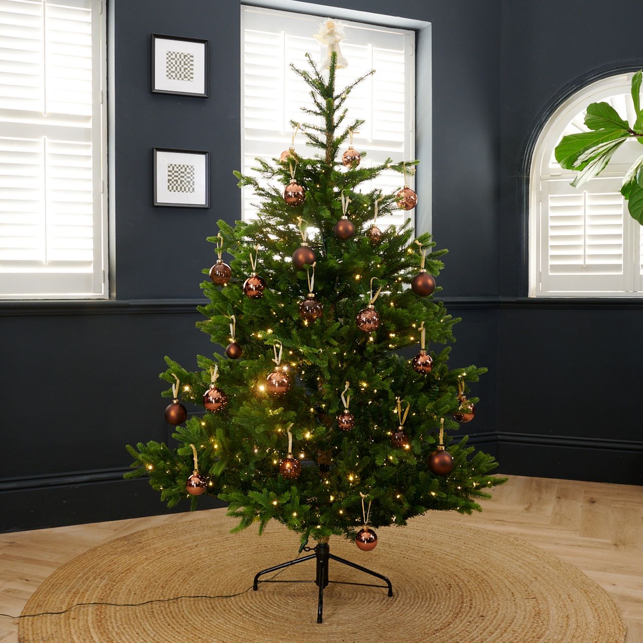 Neptune's Windsor 6ft Pre-lit Christmas Tree decorated with brown baubles set up in a black-painted living room