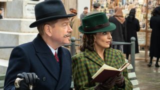 Kenneth Branagh and Tina Fey sit reviewing a book in the square in A Haunting in Venice.