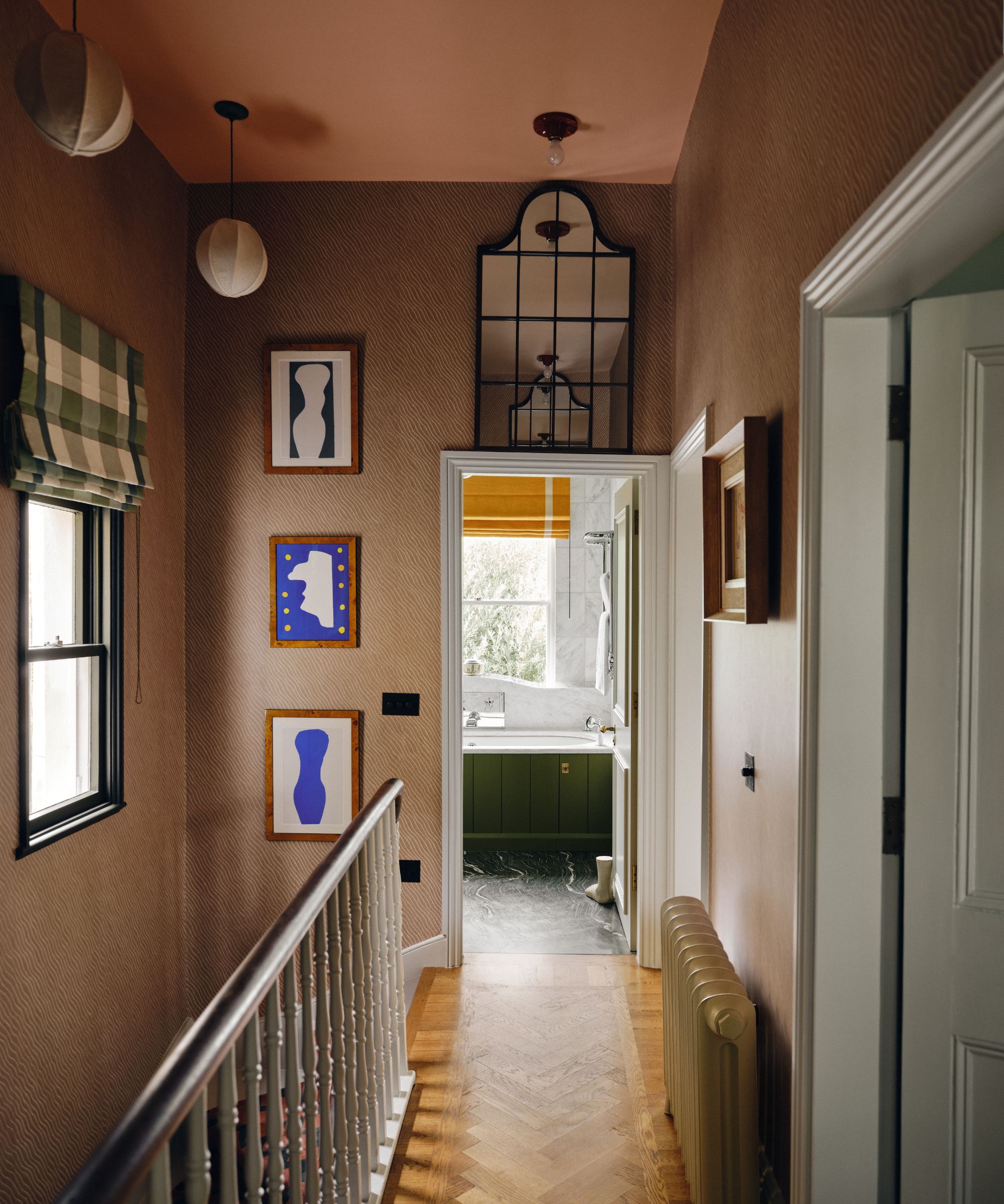 A hallway with brown wallpaper, a pink ceiling, artwork, a mirror on the wall, and parquet flooring.