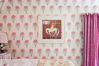 bedroom with stylised flower wallpaper, artwork, pink curtains, bedside with lamp