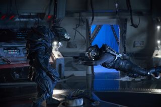 a person in a sleek black spacesuit leaps toward a standing person in similar dress inside a spaceship