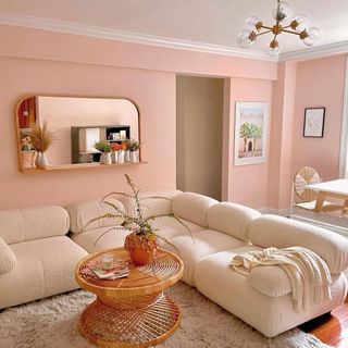 Pink F&B painted living room with boucle sectional and shug rug underneath round wicker coffee table