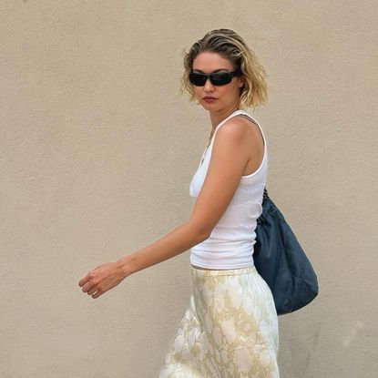 Model Gigi Hadid walking in front of a tan colored wall.