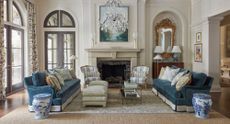 Traditional home with two rugs placed one on top of each other, blue velvet sofas, arched windows and chandelier hanging from the ceiling.