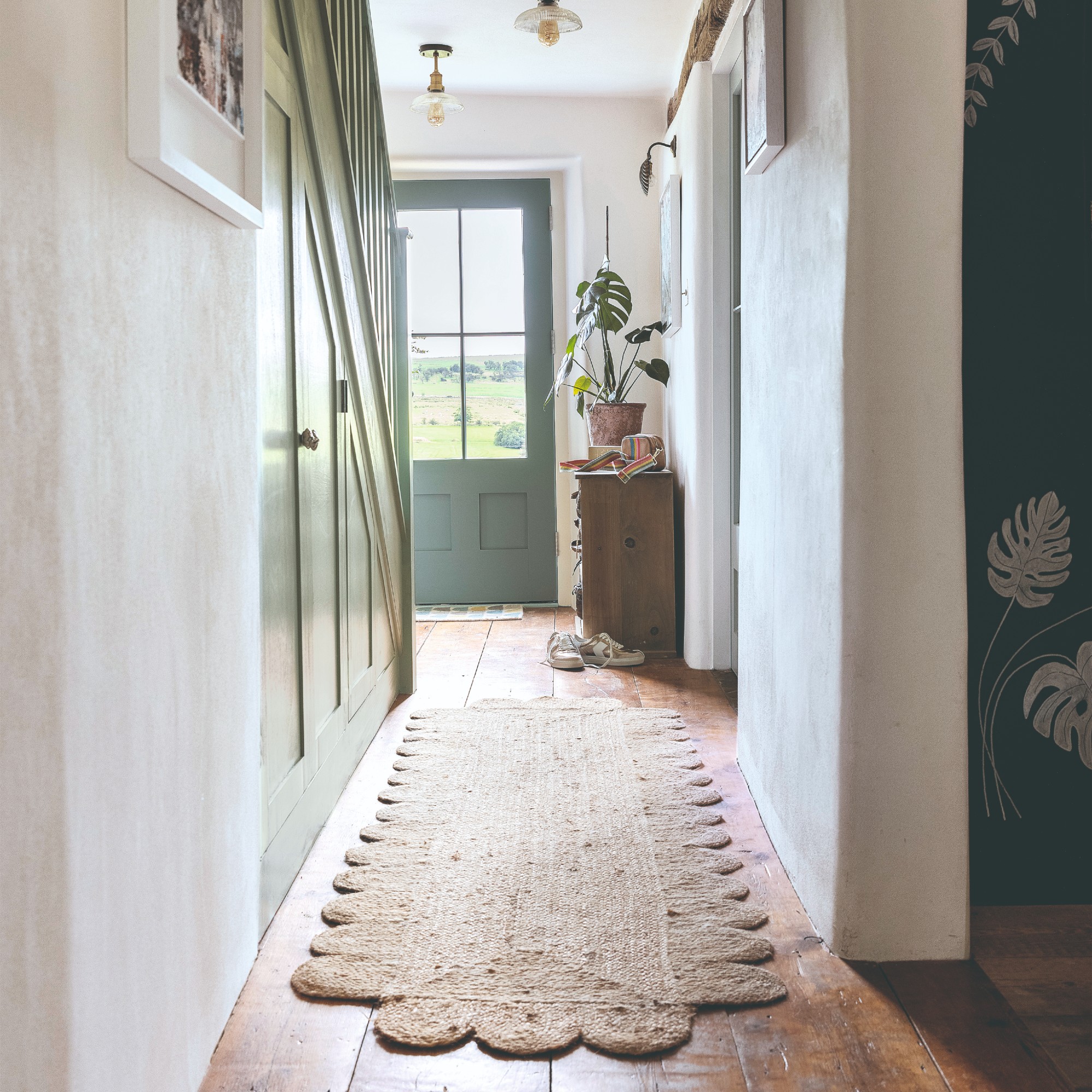A bright hallway with a jute scalloped runner and sage green front door