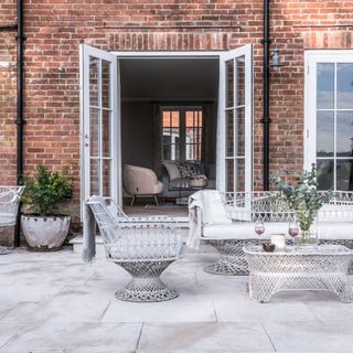 white french doors opening off living room of brick house onto patio area with ornate patio seating