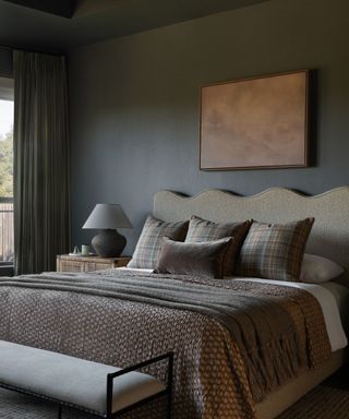 Dark grey color-drenched bedroom with wavy headboard, dark neutral bedding and bench