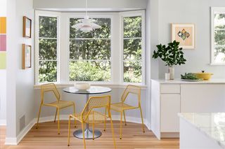 A kitchen's breakfast nook, with yellow metal chairs set in a bay window