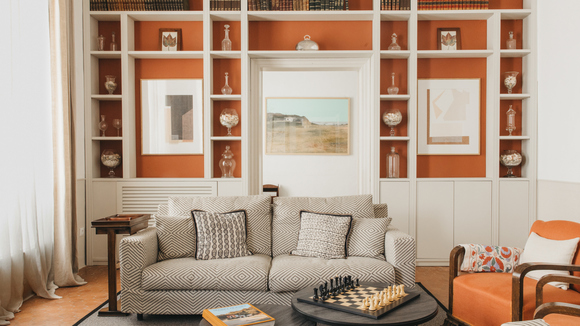 Beige sofa and orange armchairs with bookshelves behind and a table with a chess board in front, in Can Alberti 1740 hotel in Mahon, Menorca