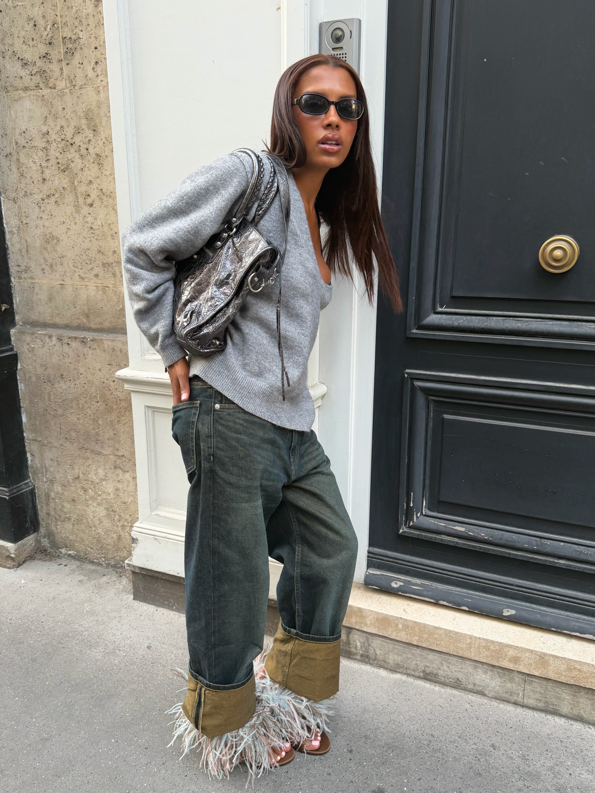 An image of a French influencer wearing a grey jumper and a turn-up jeans and holding a leather tote bag on her shoulder